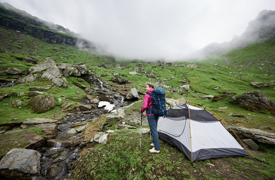Female hiker with a backpack standing near her tent in the mountains copyspace relax resting camping campsite recreation nature freedom travelling tourism hiking concept.