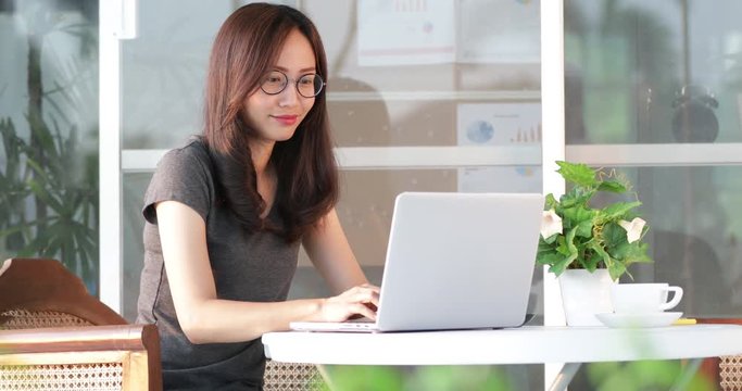 Asian Woman starts to work on her laptop and using cellphone .