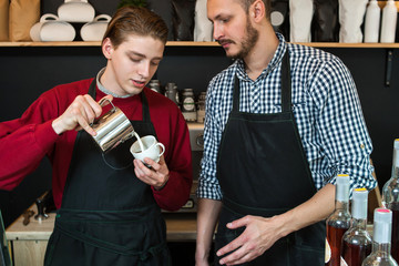 first or part time or summer job concept. professional barista teaching young man how to prepare cappuccino or latte.