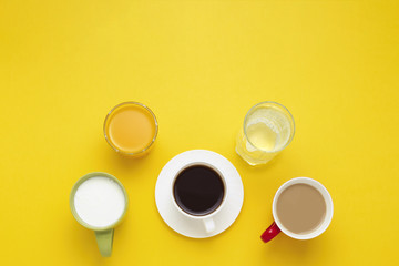 Group of Drinks in Multicolored Cups, Black Coffee, Coffee with Milk, Yogurt, Just Water, Orange Juice on Yellow Background. Flat lay, top view