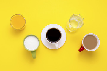 Group of Drinks in Multicolored Cups, Black Coffee, Coffee with Milk, Yogurt, Just Water, Orange Juice on Yellow Background. Flat lay, top view