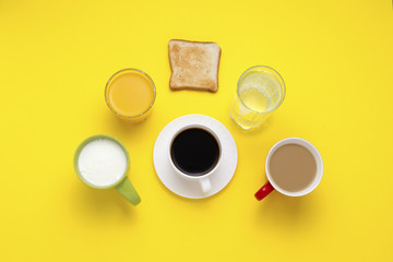 Healthy breakfast concept. Group of Drinks in Multicolored Cups, Black Coffee, Coffee with Milk, Yogurt, Just Water, Orange Juice and Toasts on a Yellow Background. Flat lay, top view