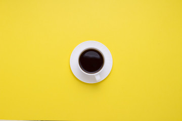 Minimalistic style. White cup with black coffee on a yellow background. Flat lay, top view