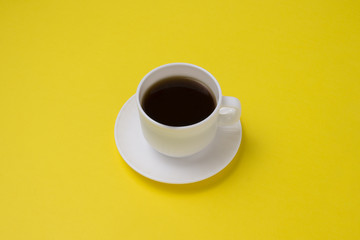 Minimalistic style. White cup with black coffee on a yellow background