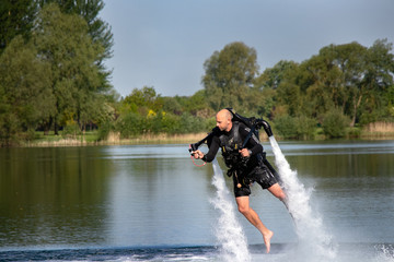 Thrillseeker, water sports lover, athlete strapped to Jet Lev, levitation hovers over lake with blue sky and trees