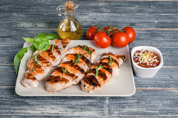 Slicers Grilled chicken fillet with herbs and tomato sauce on a wooden background.