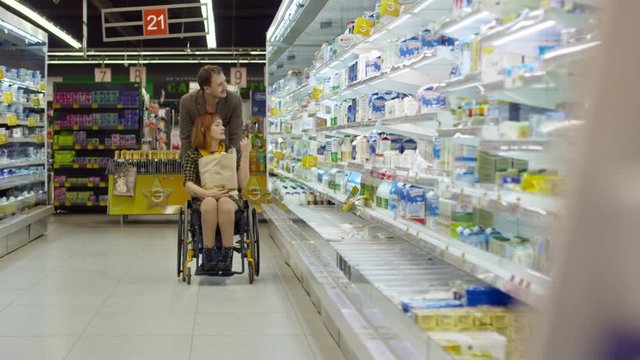 Young paraplegic woman choosing dairy products with husband; loving couple smiling and talking while going through supermarket aisle