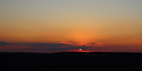 Naklejka premium Rural evening landscape - sunset at the edge of the field on the horizon with beautiful clouds in summer