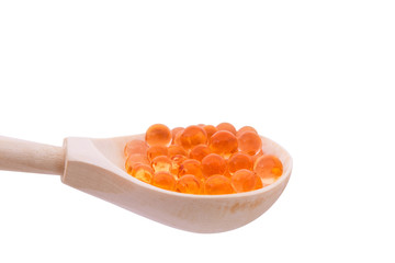 A wooden spoon with capsules similar to a red caviar on a white background,  isolated.
