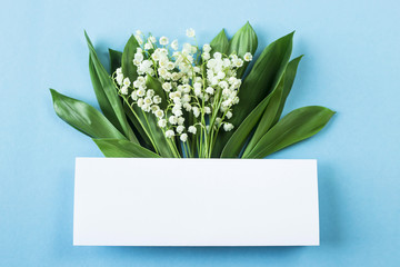 A bouquet of lilies of the valley with a white space for text on a blue background. Top view, flat lay, copy space