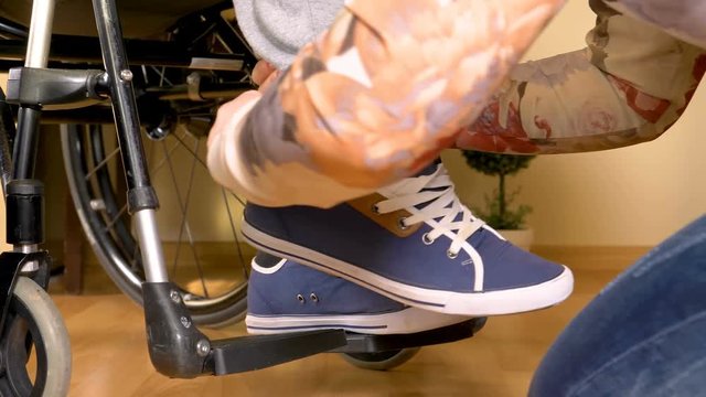 Assistance for a disabled man in wheelchair, tying shoes. Closeup 4k