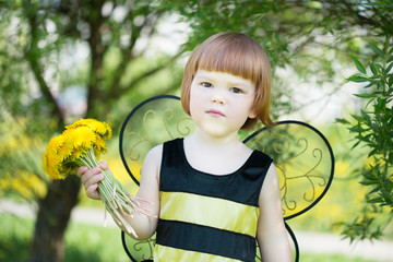 happy little girl in a bee costume walking briskly in a sunny park with dandelions