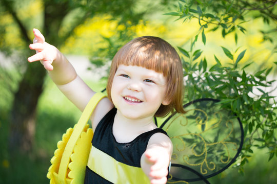 happy little girl in a bee costume walking briskly in a sunny park with dandelions