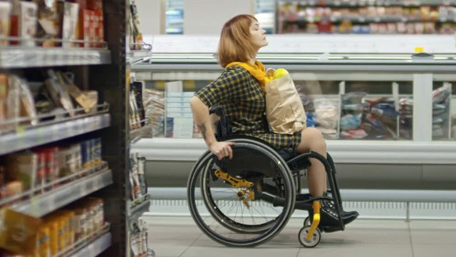 Young paraplegic woman riding wheelchair through grocery store and looking around