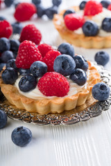  Dessert tarts with raspberries and blueberries on a wooden table.