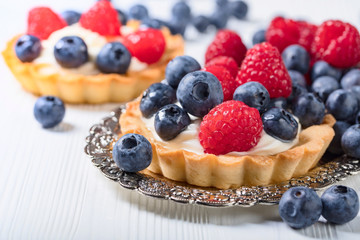  Dessert tarts with raspberries and blueberries on a wooden table.