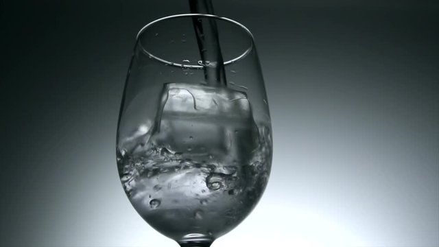 Water poured into glass with ice cubes in slow motion.  4k