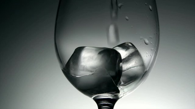 Water poured into glass with ice cubes. Macro shot slow motion 4k