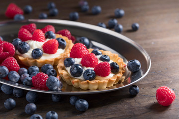  Dessert tarts with raspberries and blueberries on a wooden table.