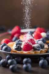  Dessert tarts with raspberries and blueberries on a wooden table.