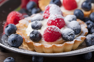  Dessert tarts with raspberries and blueberries on a wooden table.
