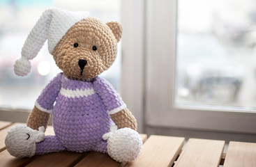 Brown stuffed animal teddy bear in lilac clothes and white hat. Copy space. Selective focus