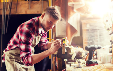 profession, carpentry, woodwork and people concept - carpenter with ruler measuring wood plank at workshop