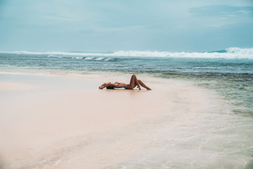 Fototapeta na wymiar gorgeous young girl in a beige bikini lies on the beach, sunbathing near the ocean. A model with a sexy body and a sports figure in the clear sea water on the island. The concept of the weekend on