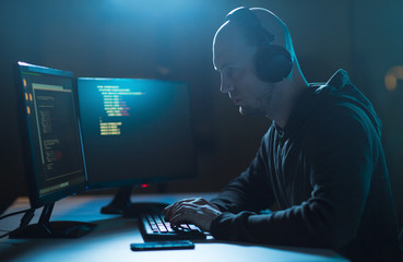 cybercrime, hacking and technology concept - male hacker with headphones and coding on laptop...
