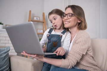 Businesswoman. Attractive happy mother sitting with her daughter and holding the laptop