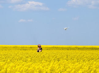 Dron flies after the girl. Shooting with a drone in the field. A girl in a black dress in a field of flowering rape