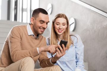 business, technology and corporate concept - smiling man and woman with smartphone at office stairs