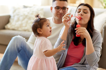family, childhood and people concept - happy mother blowing soap bubbles and playing with little daughter at home