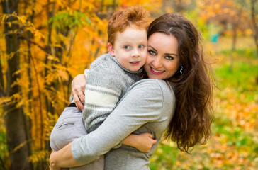 Fototapeta premium Happy family: mother and child sonr have fun in autumn on autumn park. Young Mother and kid girl hugging in leaves at fall.