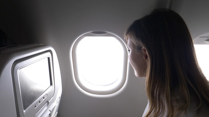 CLOSE UP: Smiling businesswoman looking through the window of transatlantic jet.
