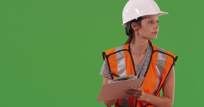 Female construction worker writing notes on clipboard on green screen
