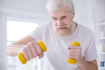 I love boxing. The close up of a handsome elderly man in a white t-shirt practicing boxing kicks while working out in the morning