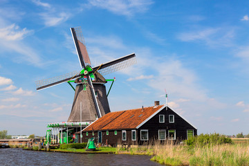 Fototapeta na wymiar Dutch typical landscape. Traditional old dutch windmill with house blue sky in the Zaanse Schans village, Netherlands. Famous tourism place.
