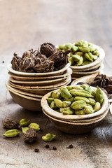 Black and green cardamom whole seed in coconut bowls on wooden background