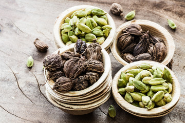 Black and green cardamom whole seed in coconut bowls on wooden background