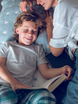 Mother sleeping and son reading book on bed