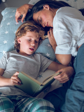 Mother sleeping and son reading book on bed