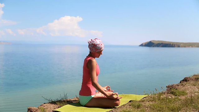 Professional yoga woman practices yoga moves outdoors. Girl is meditating. blue lake baikal on the background