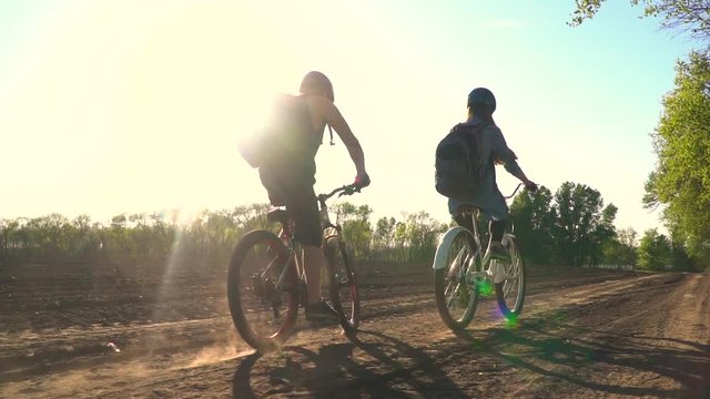 Slow-motion shooting as a pair of cyclists drive along a dirt road next to the trees