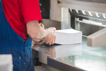 Hands of worker in typography puts the paper stack in the cutter