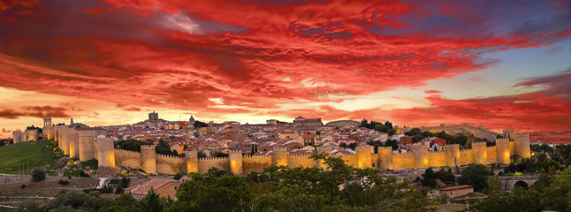 Walls of Medieval city of Avila at sunset with lights on, Spain