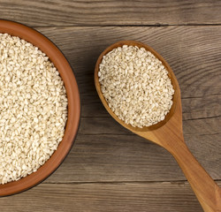 Sesame in a bowl on wooden background with a wooden spoon