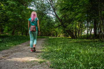 Obraz premium soft focus young girl with pink hair and green clothes walking in park back to camera