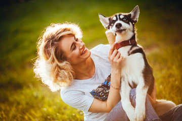 owner is smiling and feeding her dog by ice cream on the meadow in the park