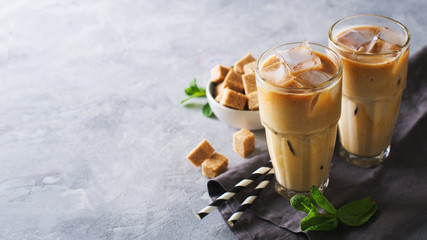 Iced coffee in tall glasses with cream and pieces of sugar, mint and straw - obrazy, fototapety, plakaty